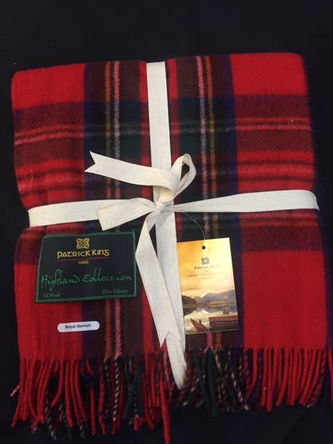 A Royal Stewart Deluxe Highland Blanket in red tartan merino wool, with fringe edges, folded and tied with a white ribbon, features Patrick King Highland Collection and Royal Stewart labels.