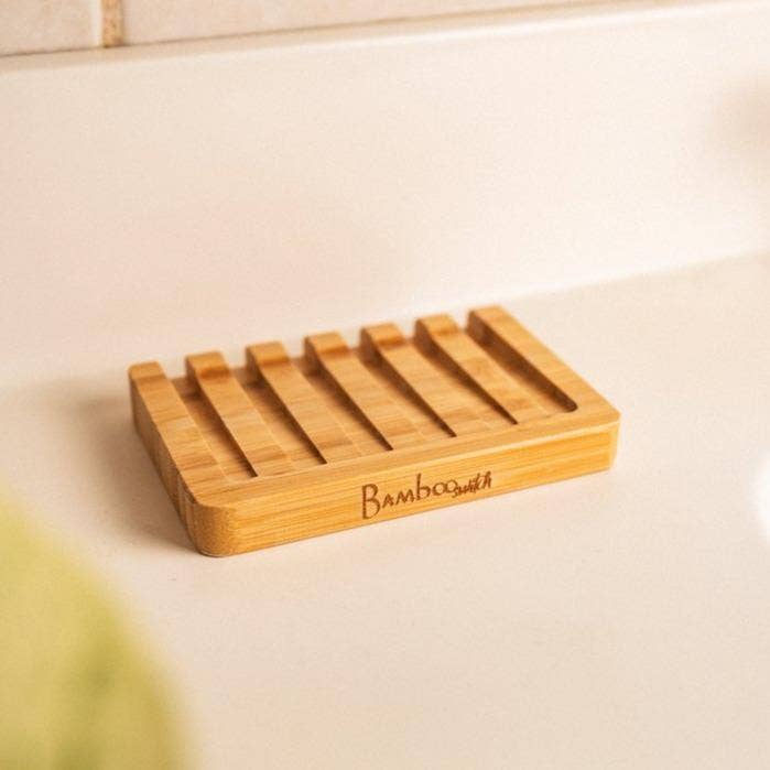 The Soap Dish: Bamboo Soap Lift, a rectangular holder with grooves, rests on a white countertop—an eco-friendly and sustainable bathroom accessory for holding soap.