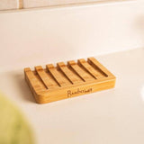 The Soap Dish: Bamboo Soap Lift, a rectangular holder with grooves, rests on a white countertop—an eco-friendly and sustainable bathroom accessory for holding soap.