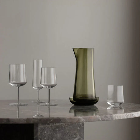 An Orrefors Informal Carafe with Bowl (Olive) is arranged on a round marble table against a plain grey background, highlighting the timeless elegance of Orrefors craftsmanship.