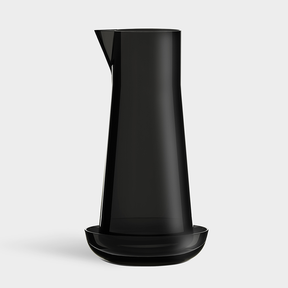 The Orrefors: Carafe with Bowl features a tall, black carafe designed by Björn Dahlström, paired with a matching shallow bowl and photographed against a plain light background.