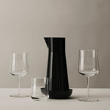 The Orrefors: Carafe with Bowl, in black, sits empty on a white surface between a short glass and two wine glasses, all against a neutral background.