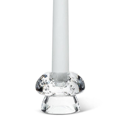 A white candle stands upright in the Mushroom Glass Taper Candle Holder, which measures 2" tall by 2.5" in diameter and features a rounded, textured base inspired by mushroom decor.