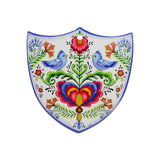 The Tile: Lovebirds Folk Art Cork Backed Ceramic Shield is a Nordic-designed wall decor featuring blue birds, vivid flowers, and symmetrical patterns—an ideal Swedish novelty gift to bring folk art charm to your home.