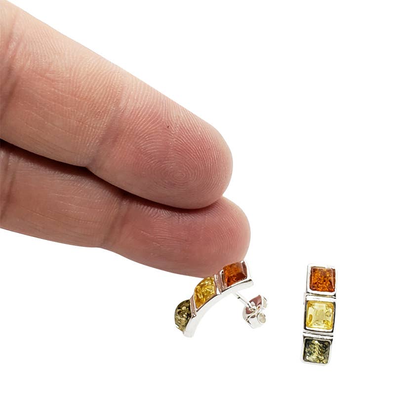 A hand holds a curved earring embellished with square, multicolored stones in sterling silver, alongside its matching straight counterpart on a white backdrop; these are the Multi Color 3 Amber Stones with Sterling Silver Stud Earrings.