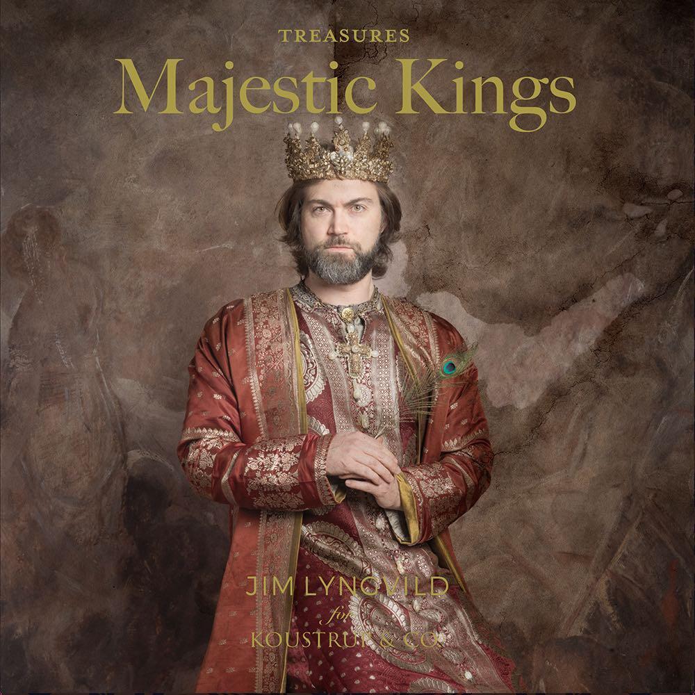 A man dressed in regal attire and wearing a crown stands against a textured backdrop reminiscent of Christmas motifs. The text reads "Card Pack: Majestic Kings by Jim Lyngvild," printed on eco-friendly paper.