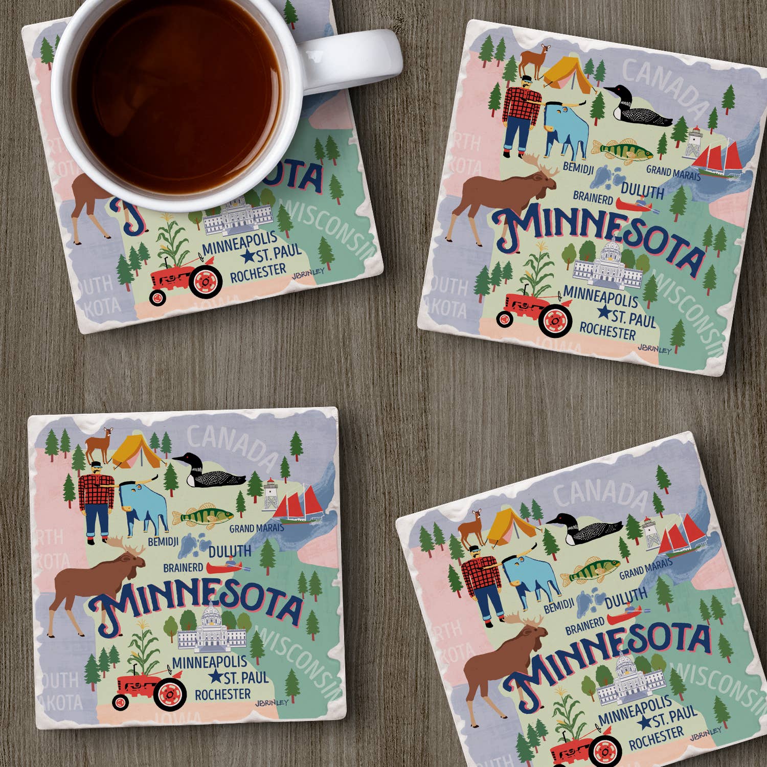 A steaming cup of coffee sits on a wooden table alongside four Minnesota Attractions Thirstystone Coasters with cork backing, showcasing colorful illustrations of landmarks, wildlife, and city names.