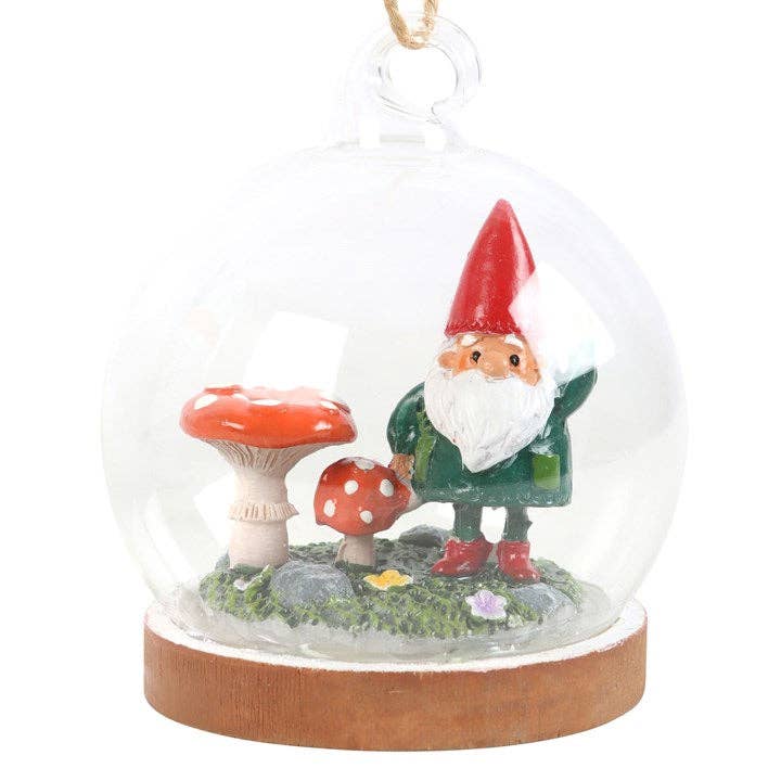 The "Ornament: Gnome Glass Dome" showcases a charming gnome in a red hat, standing next to two red mushrooms, all beautifully encased in a glass dome resting on a sturdy wooden base.