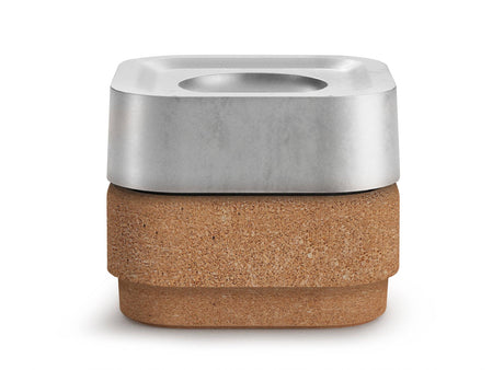 The Stumpastaken Ettan candle holder, crafted from 100% recycled aluminum with a white powder-coated finish (8.8x8.8x4 cm), sits on a cork base, both featuring rounded edges and a minimalist design, highlighting sustainability.