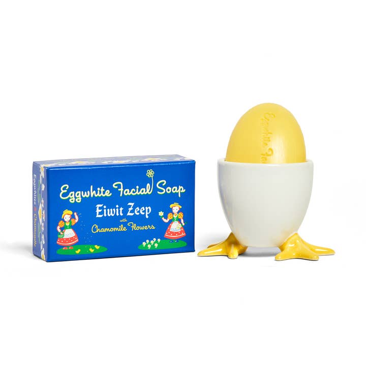 A box labeled Soap: Eggwhite & Chamomile Facial Soap – 2.25 oz sits beside an egg-shaped gentle daily cleanser in a white holder with yellow feet.