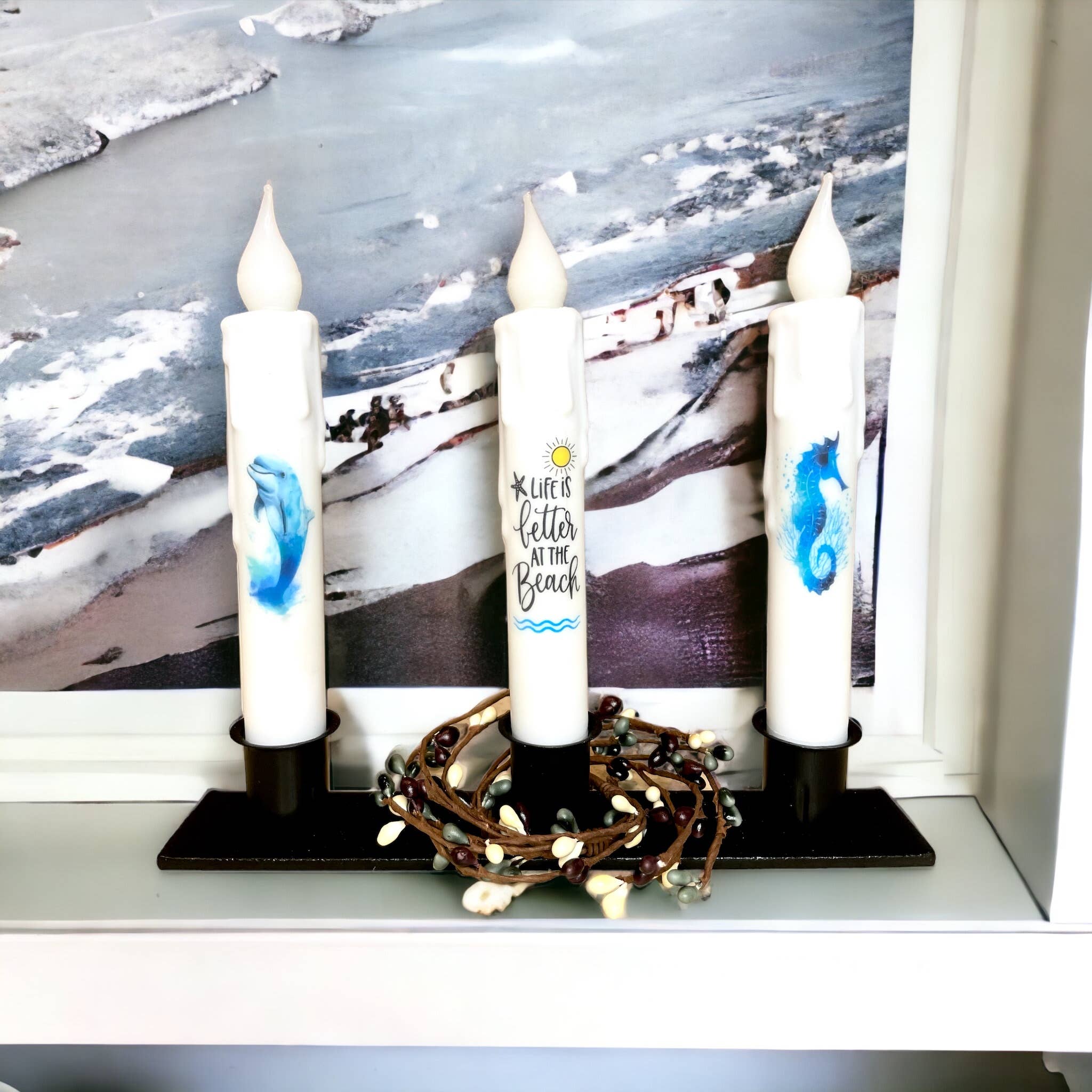 Featuring the Candle Holder: Triple Wrought Iron Taper Holder, this set includes three white candles adorned with blue marine designs and the text "Life is Better at the Beach." Ideal as a centerpiece, these candles beautifully capture the essence of coastal living.