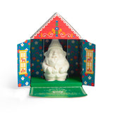 White chocolate gnome inside a colorful, house-shaped box with Nordic floral patterns and open doors.