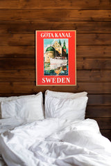 A wooden wall displays a 50 x 70 cm Scandinavia Travel Poster Göta Kanal Vadstena above an unmade white bed, printed on high-quality matte paper.