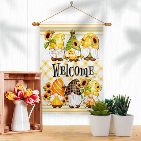The Flag: Spring Gnomes Garden Floral Gnome Decor Flag, featuring cartoon gnomes, sunflowers, and WELCOME, is displayed above a wooden box of flowers and two small potted succulents.