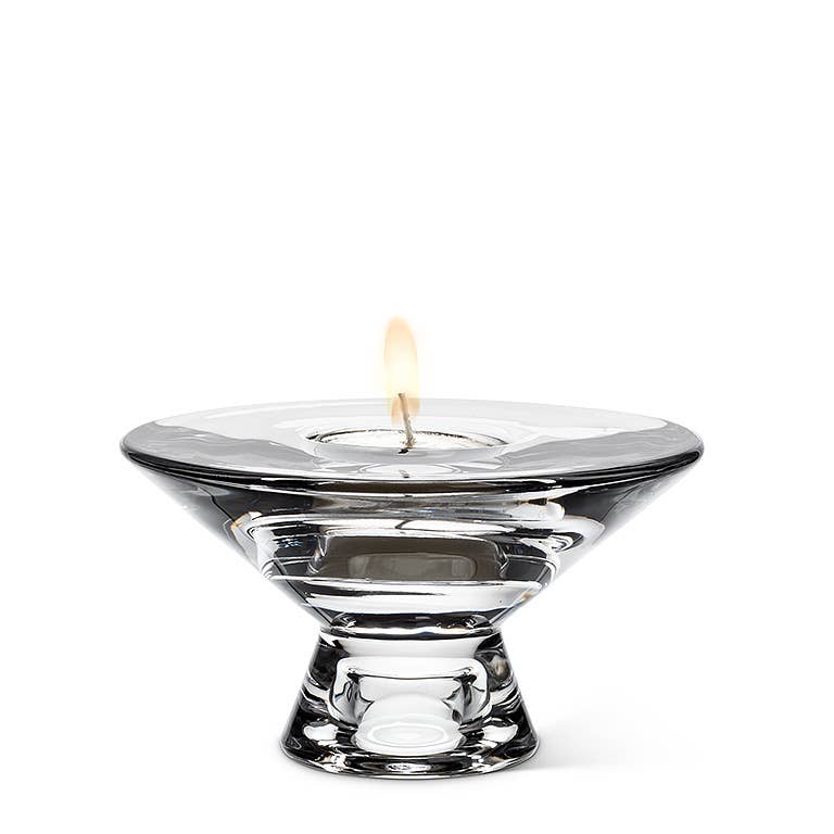 The Reversible Glass Candleholder (4.5" D) features a sophisticated design with a glass holder and lit flame on top, making it ideal for adding a warm and inviting glow to any environment.