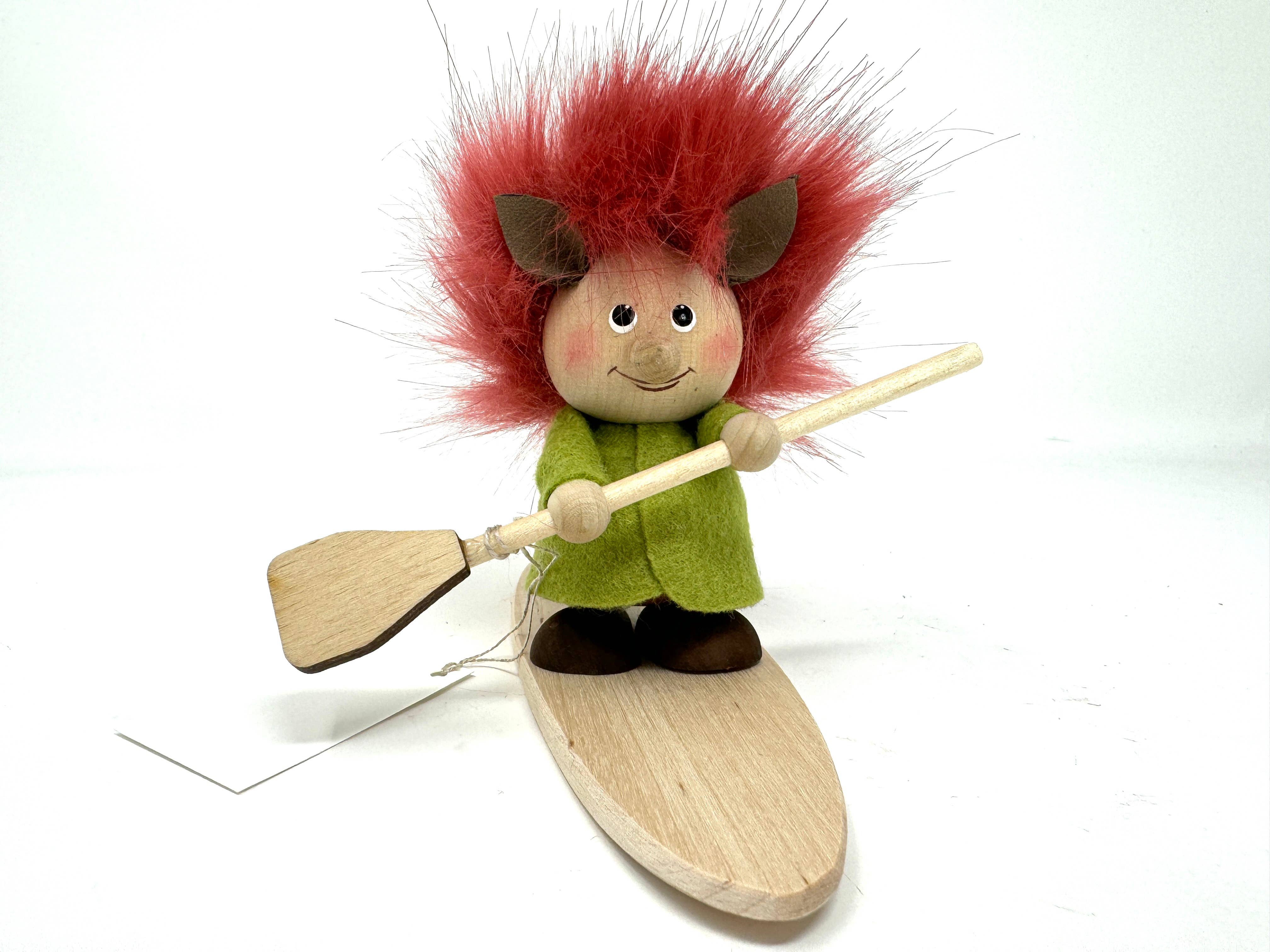 The Troll with Paddle Board figurine is handcrafted with red fuzzy hair, dressed in a green outfit, and stands on a wooden platform holding a paddle board.