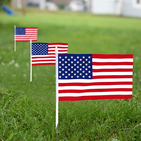 Three USA United States Mini Flags (5x8) on white sticks stand in a row on green grass, their fade-resistant colors vivid against a blurred yard—perfect handheld American flags for patriotic events.