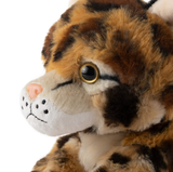 Close-up of a plush toy cat with brown, black, and white fur, golden eyes, pink nose, visible whisker spots, facing slightly left.