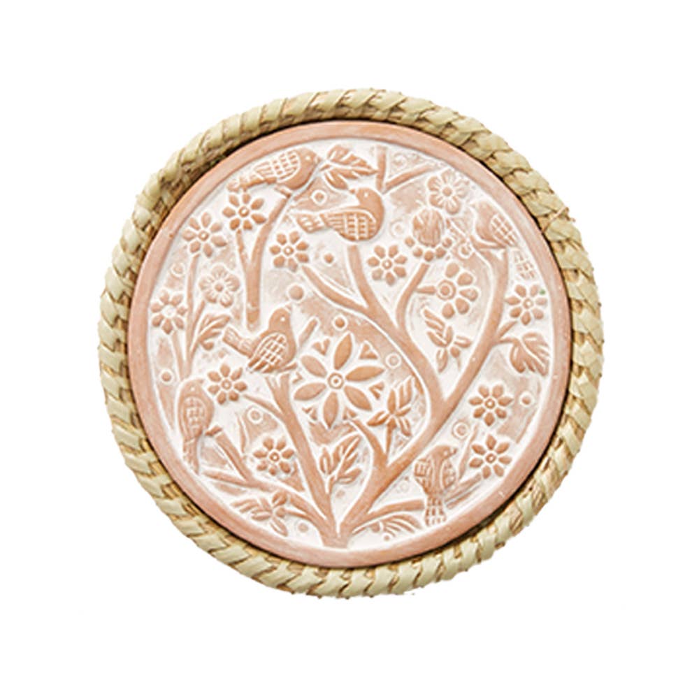 The Birds of a Feather terra-cotta warming trivet features a raised floral and bird design with woven straw trim, making it an ideal decorative piece.