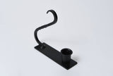 Black iron taper holder with a rectangular base, circular candle cup, and an arched handle with twisted metal detail.