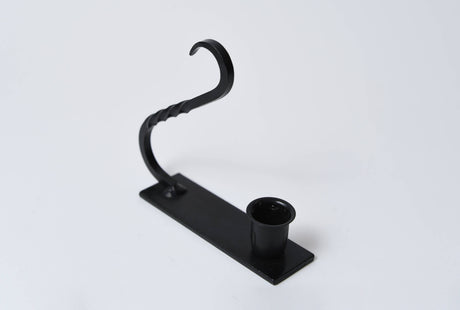 Black iron taper holder with a rectangular base, circular candle cup, and an arched handle with twisted metal detail.