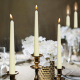 Three 10 inch unscented taper candles from the White, Red, or Ivory Tall Taper Candles 4 Pack sit in brass holders amid white flowers and glassware, creating an elegant and formal atmosphere with dripless charm.