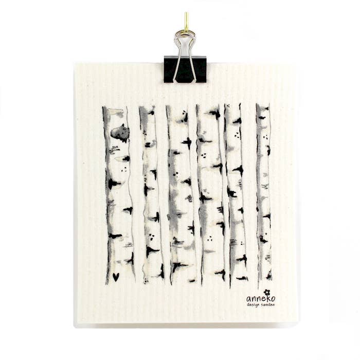 A clip securely holds the Dish Cloth: Birch Trees by Anneko of Sweden, which features a black and white drawing of birch trees on eco-friendly, compostable material.