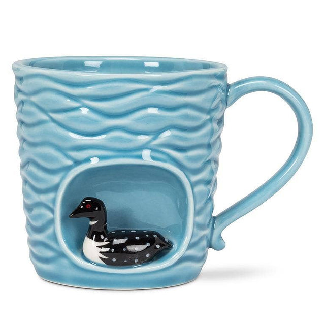 The Wavy Aqua Mug with Loon in Recess (4"H, 14oz) features handcrafted ceramic, a textured wave pattern, and a detailed black-and-white loon figurine near the base—making it an ideal nature-inspired gift.