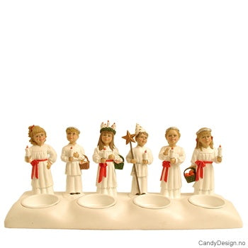 The Candle Holder: St Lucia Train features six porcelain figurines dressed in white with red sashes, each holding different objects like baskets and candles, standing in a row on a base.