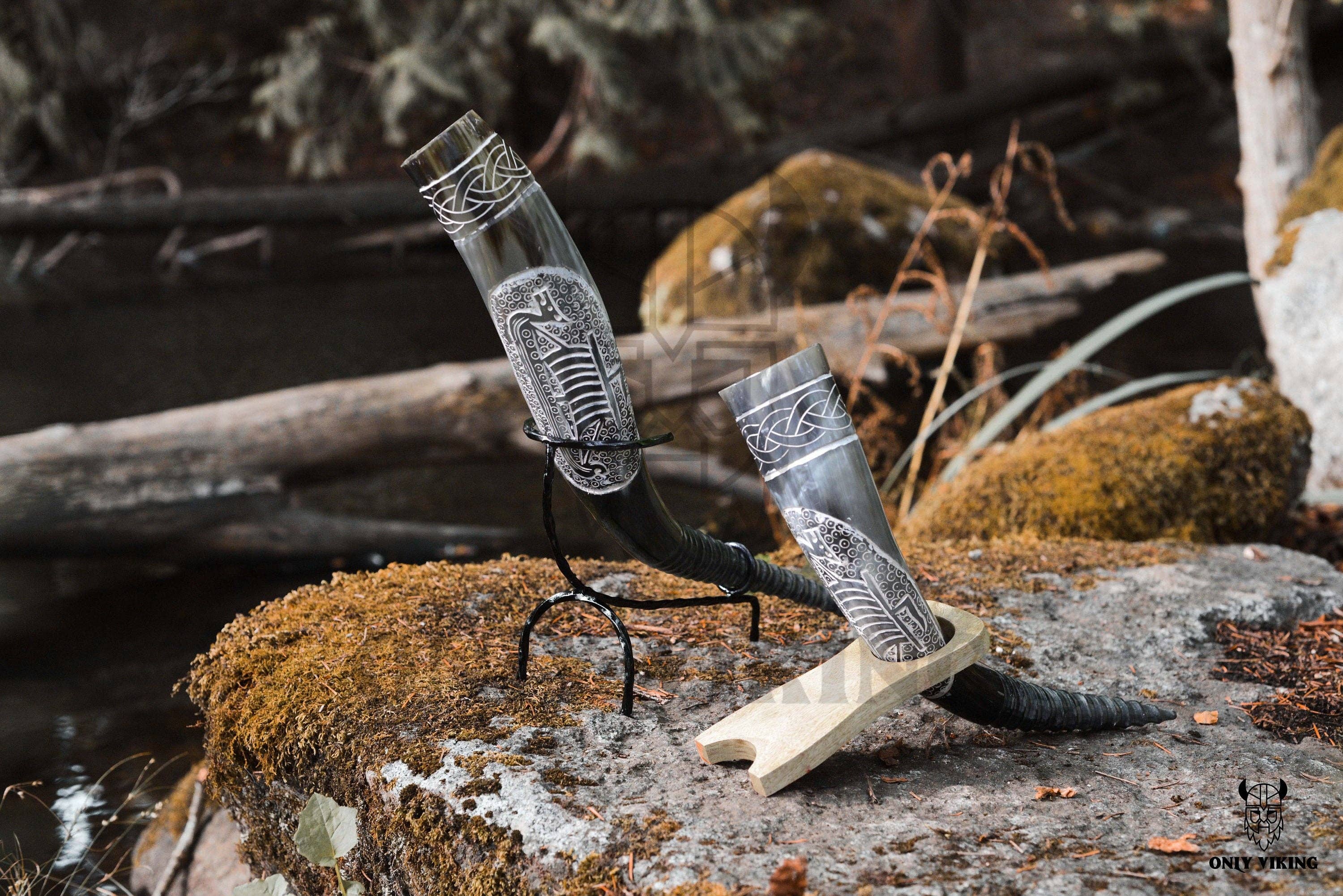 Two Ravens Viking Ship Handcrafted Drinking Horns (14-18) with metal stands rest on a mossy rock against a forest backdrop.