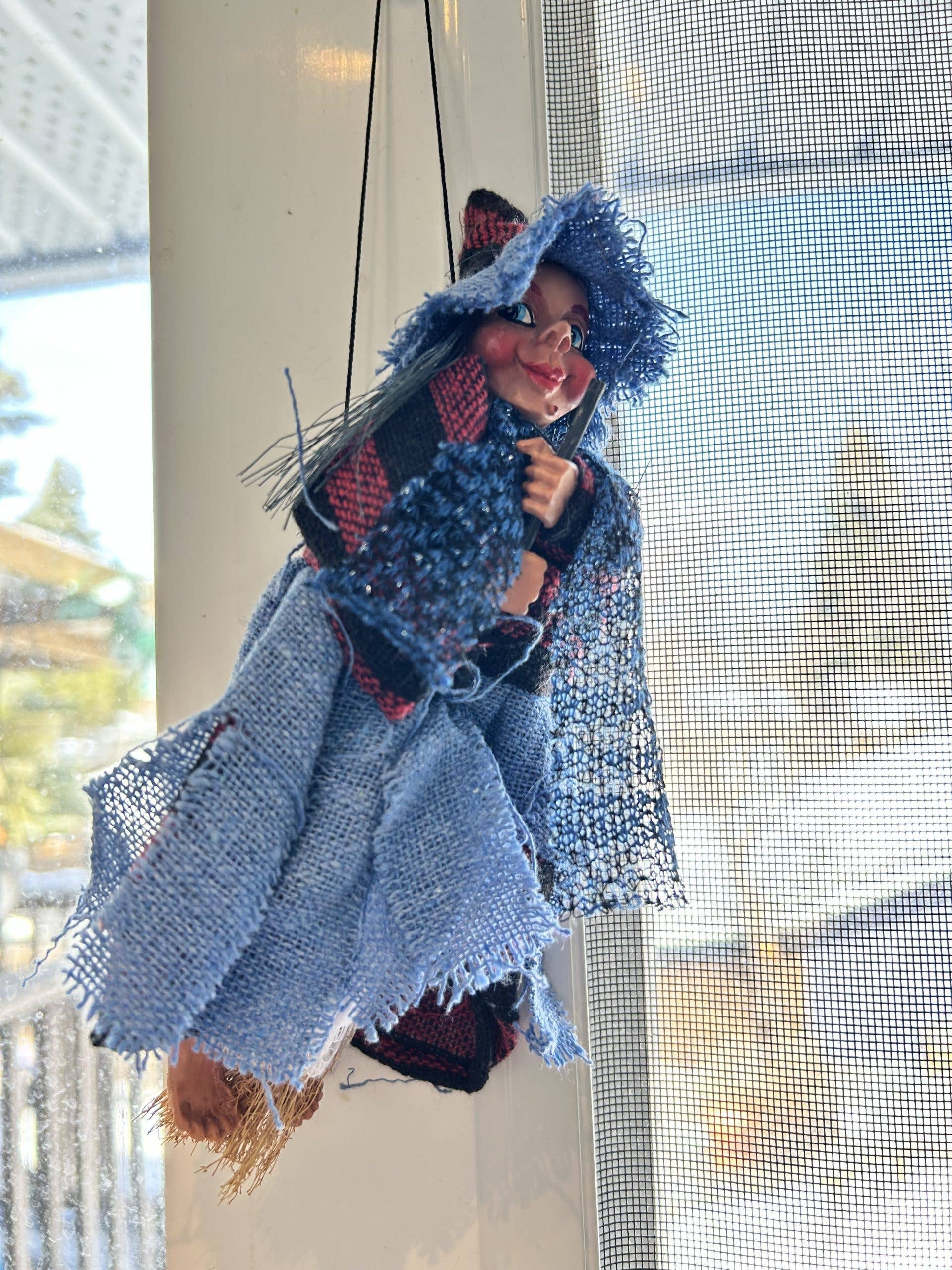 The Philippa Blue Kitchen Witch Doll is a handmade German charm, dressed in blue and hanging by strings, perfect for bringing good luck to your kitchen.