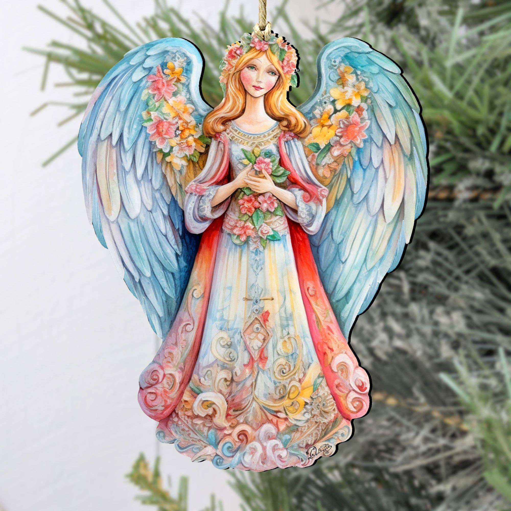 The Angel Blue Floral Wooden Ornament from Debrekht, hanging on a Christmas tree branch, adds charm to your Nativity holiday décor with its colorful wings and floral details. This exquisite handcrafted keepsake embodies timeless elegance.