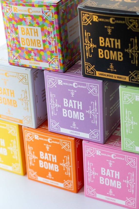 A stack of colorful bath bomb boxes, featuring Coconut Island and other scents like Rambling Caravan, Celebrate, and Lavender, arranged in rows to offer a luxurious and skin-nourishing bath experience.