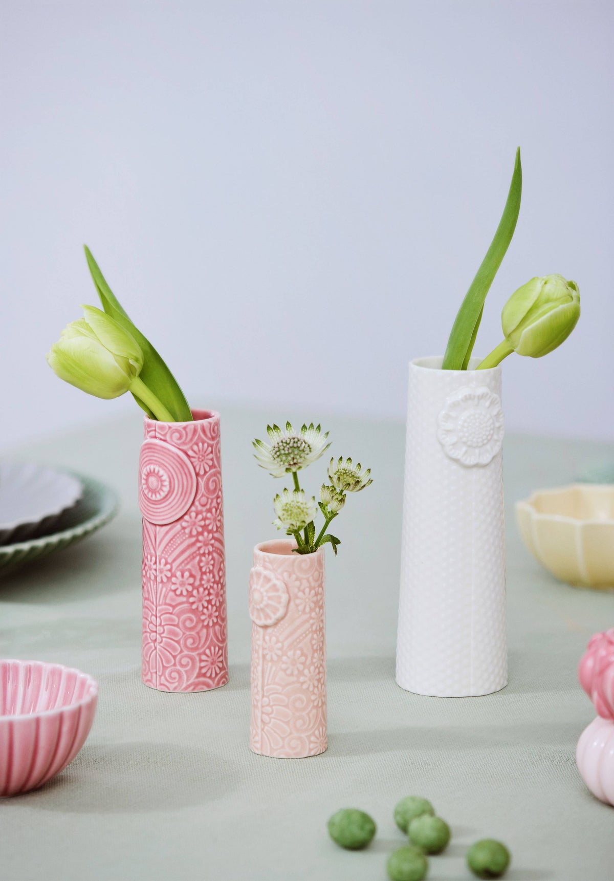 Three handmade Nordic ceramic vases in pink, light pink, and white with embossed floral patterns, holding fresh flowers.