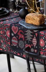 Black tea towel with a red, white, and grey pattern of hearts, Dala horses, and flowers, shown under a loaf of seeded bread on a black board.