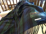 A Black Watch Highland Tartan Plaid Wool Blanket (69"x62") in dark green and navy, with fringed edges, is draped over a white surface. The label reads Patrick King Highlands Collection.