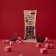 A 2 oz packet of Wally & Whiz US Danish Sweets Cherry with Sour Cherry Vegan Gummies stands upright on a red surface, surrounded by scattered gummies and fresh cherries against a solid red background.