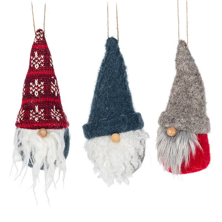 The Gnome Ornament (6"H) set includes three plush ornaments with pointy hats in red, blue, and gray. Each gnome features a white beard and wooden nose, making them perfect for holiday decor. They hang charmingly on strings.