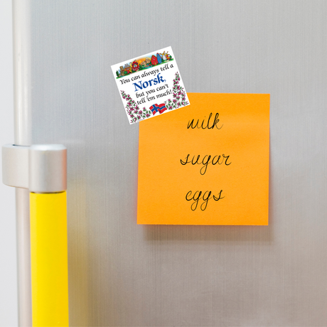 Orange sticky note on a fridge with handwritten list: milk, sugar, eggs. Above it, a Scandinavian souvenir magnet featuring floral designs and text.