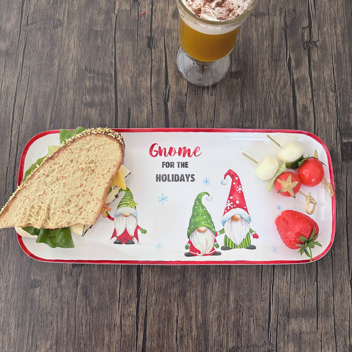 Melamine tray with sandwich, skewered cheese and tomatoes, strawberry, gnome illustrations, and “Gnome for the Holidays” text; coffee cup visible in background.