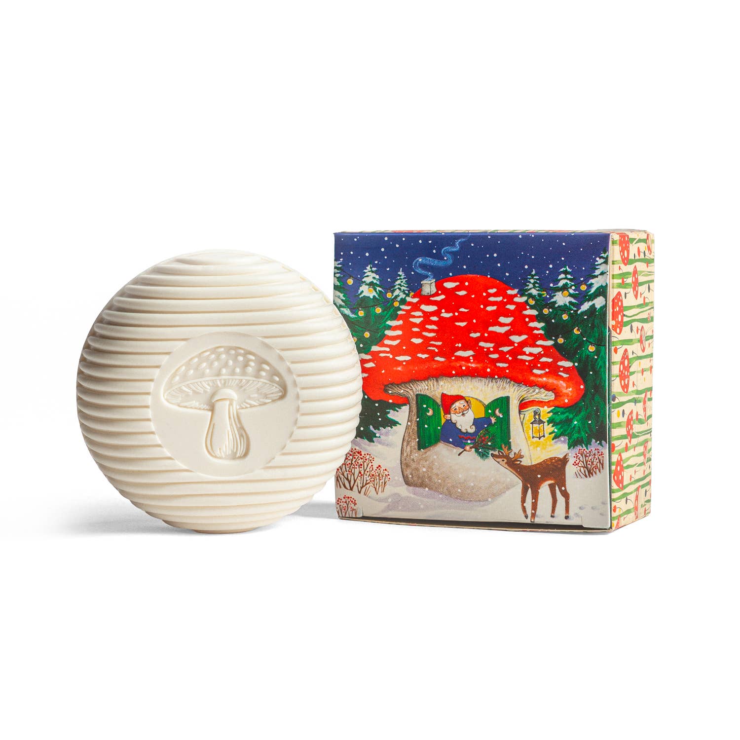 The Soap: Gnome Soap Swedish Pine Swedish Dream Bar Soap is a round white soap with a mushroom design, paired with a vibrant box showing a gnome, mushroom house, and deer in a snowy forest. Plastic-free for whimsical charm.