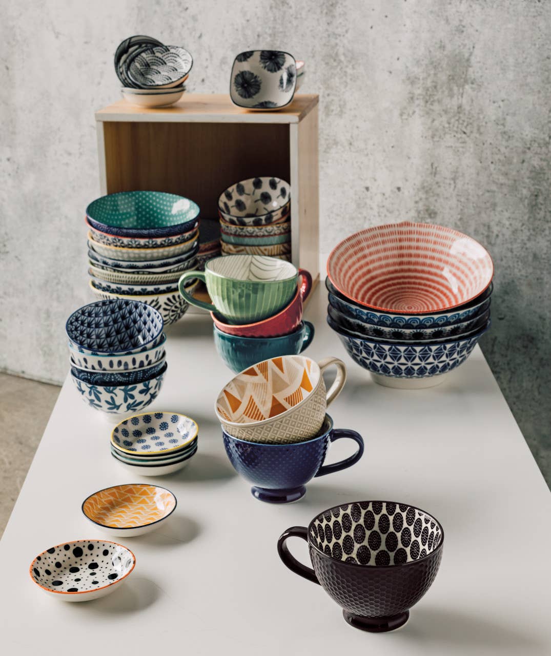 A collection of vibrant, patterned ceramic bowls and plates is showcased on a white surface and wooden shelf in a charming cottage chic style, featuring the delightful Navy Bird Stamped Bowl, measuring 6 inches.