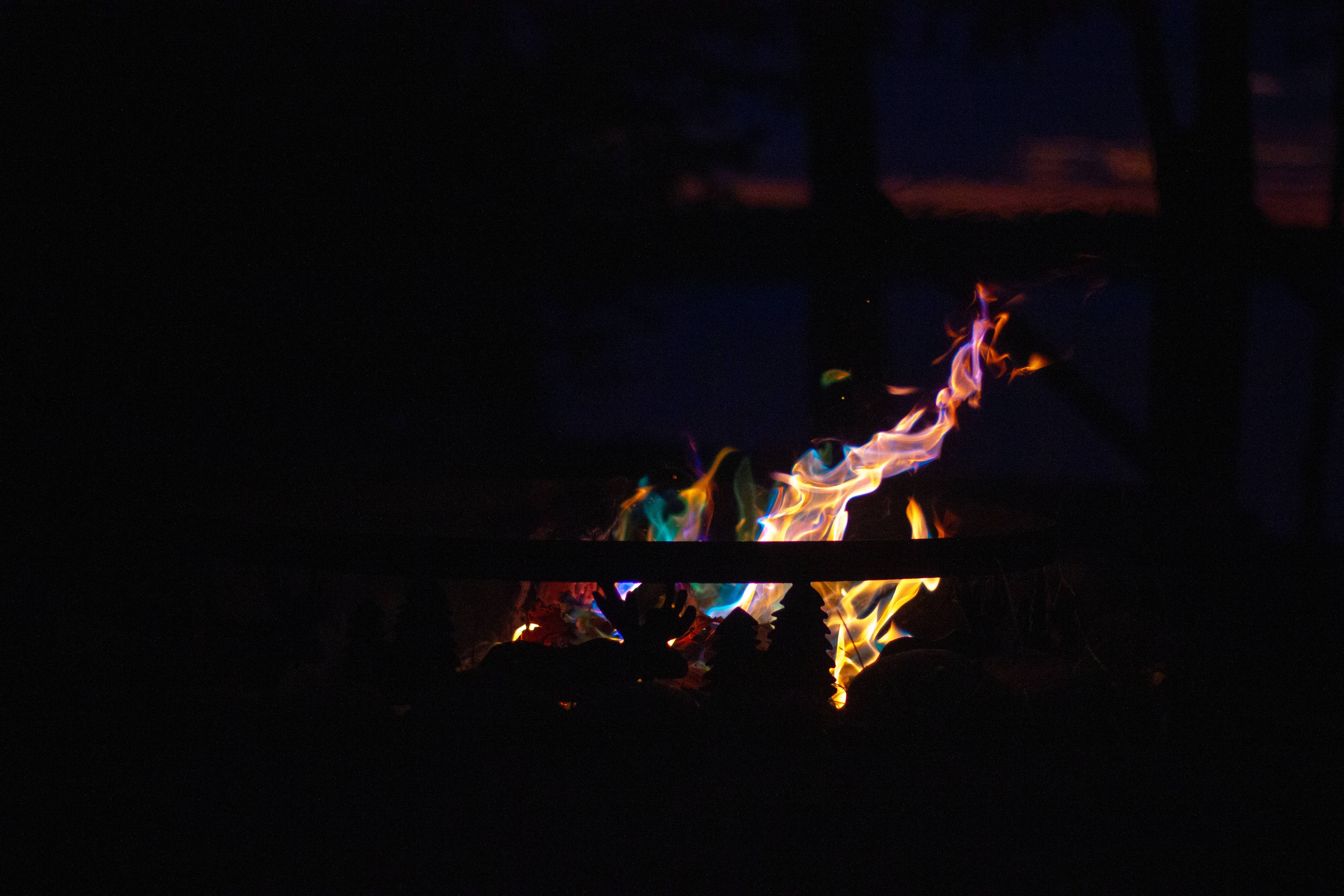 A campfire fueled by Fire Color Cones: Northern Lights - Fire Color Cones (Small Refill Pack) dances with multicolored flames, displaying blue, green, and orange against the dark night background.