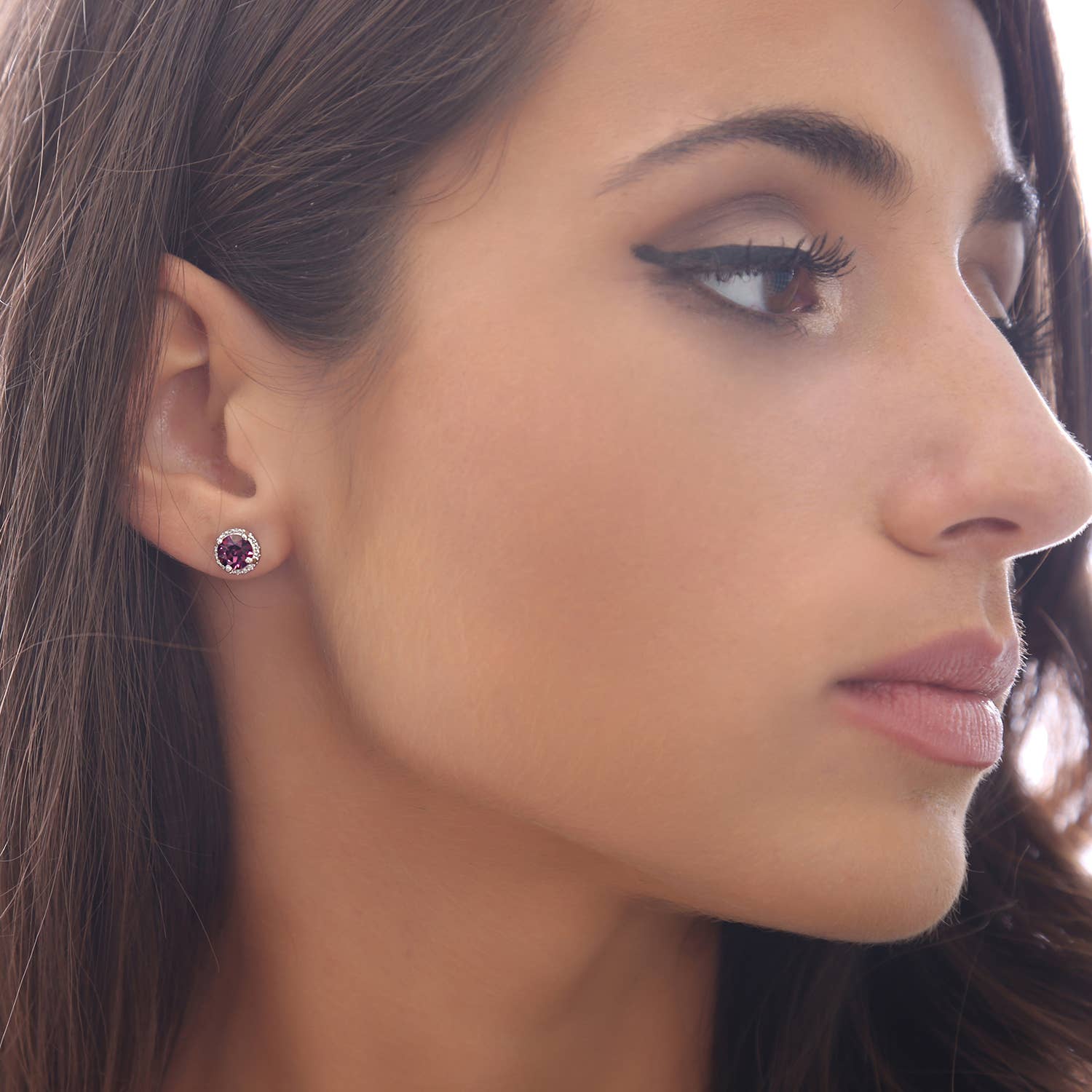 A woman with long brown hair and winged eyeliner wears handmade silver solitaire stud earrings featuring garnet red Swarovski crystals.