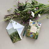 The Card Pack: Anne Just Cardfolder includes 8 garden-design cards with envelopes, shown alongside wildflowers, a postcard, and a green pen on a light gray surface.