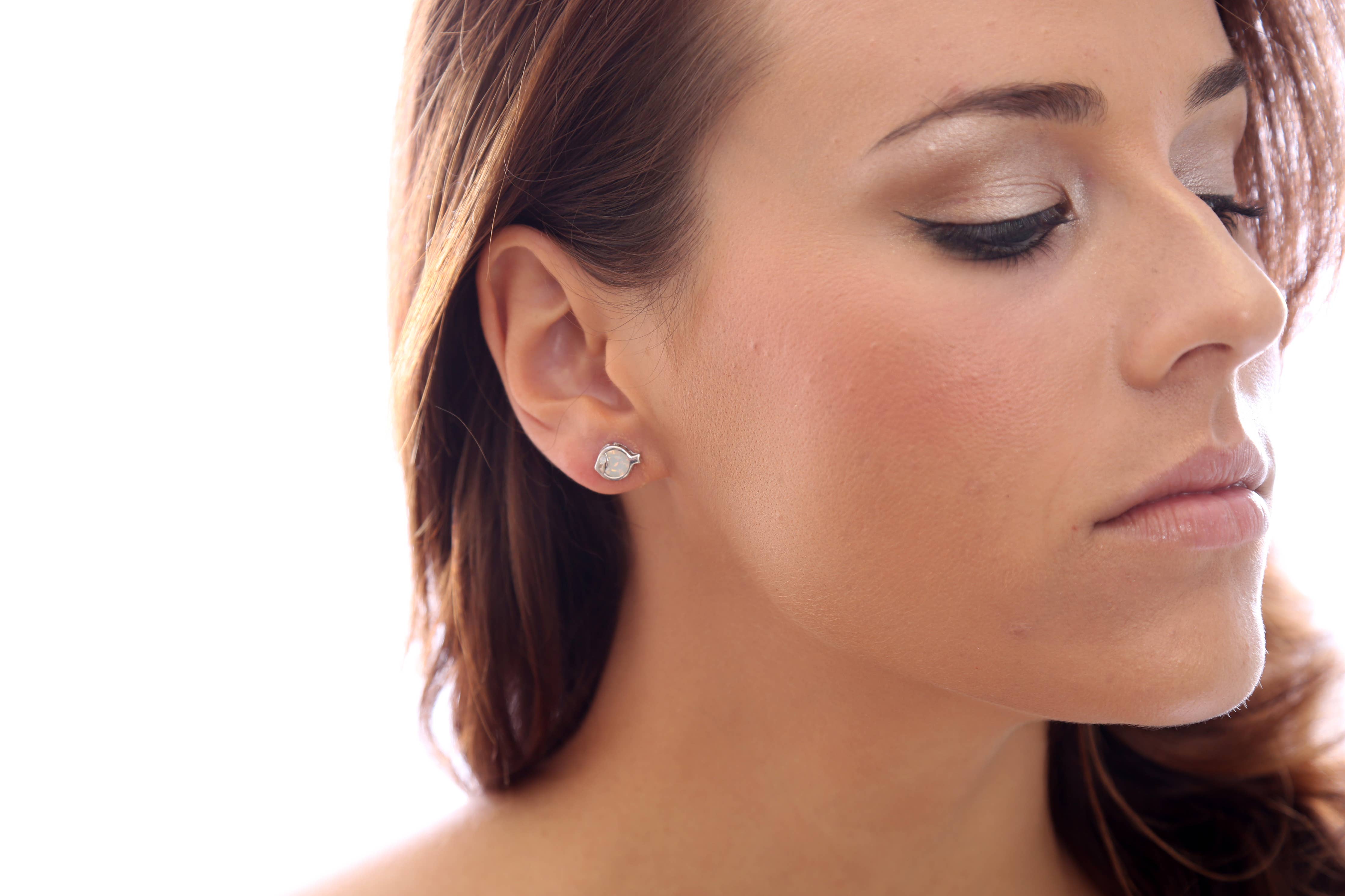 Close-up of a womans profile with neutral makeup, eyes closed, and hair partly visible. She wears sparkling Fish Shaped Swarovski® Crystal Silver Stud Earrings.