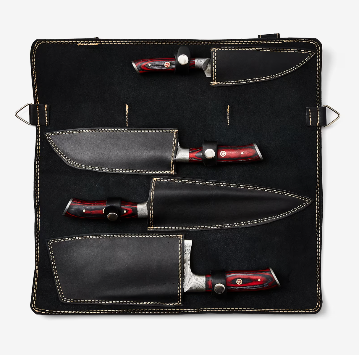 Set of four Damascus steel knives with red and black handles, each in a black leather sheath, laid out on a fabric roll with beige stitching and securing loops.