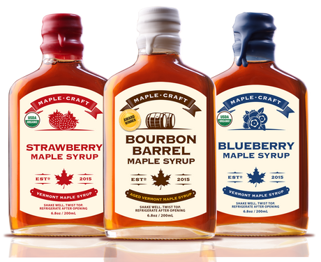 Three bottles of organic, refined sugar-free maple syrup stand side by side with labels: Strawberry - Summer Favorites Maple Syrup (6.8 oz), Bourbon Barrel, and Blueberry. Each features a maple leaf insignia and the year 2015.