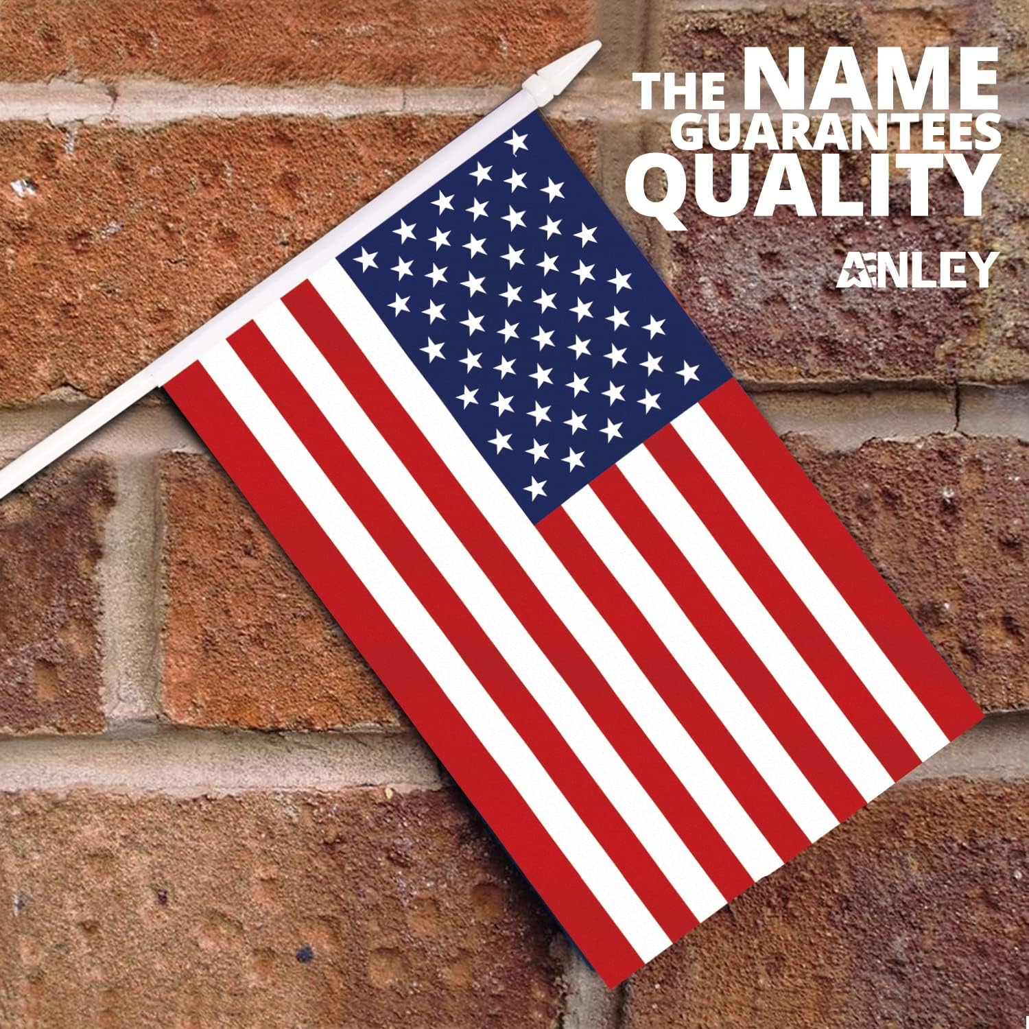 A USA United States Mini Flag (5x8) with fade-resistant colors on a white stick is mounted on a brick wall. The top right corner displays: THE NAME GUARANTEES QUALITY ANLEY.