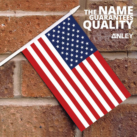 A USA United States Mini Flag (5x8) with fade-resistant colors on a white stick is mounted on a brick wall. The top right corner displays: THE NAME GUARANTEES QUALITY ANLEY.
